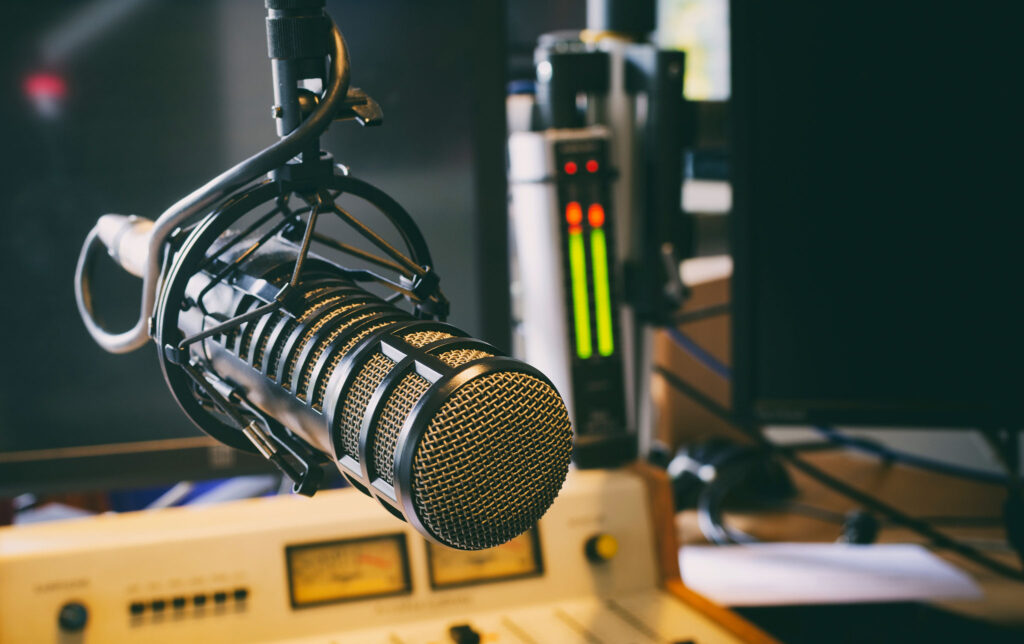 Fotografia do estúdio de rádio, mostrando a mesa de canais e o microfone usado pelo locutor, representando a infraestrutura de uma rádio comunitária