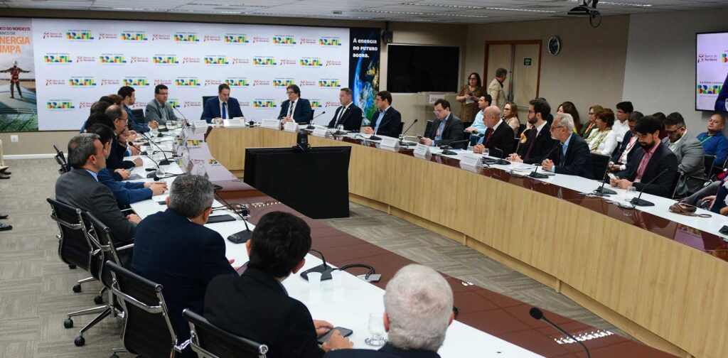 Sala de reuniões na sede do BNB. Sentados à mesa, membros do governo Lula e dirigentes do Banco do Nordeste. Ao fundo, um painel com a logomarca do banco e do governo federal.